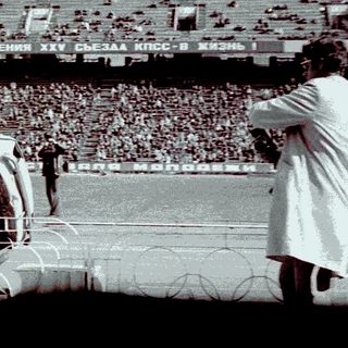 Man standing on car, raising arm in stadium setting.