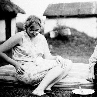 Here's a brief summary of the image: Two women seated outdoors, appearing to be making something.