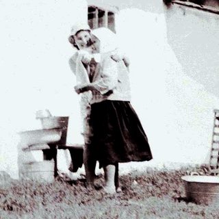 Here's a brief summary of the image: Two women stand outside a house in a rural setting.