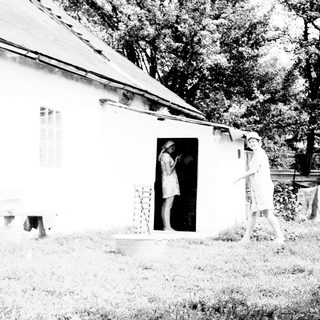 Two figures near a house with laundry hanging outside.