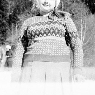 Girl in winter clothes stands in a snowy, wooded landscape.