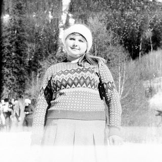 Girl in winter clothes stands in a snowy, wooded landscape.