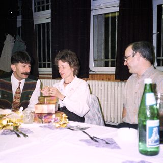 Three people seated at a table, gift exchange.