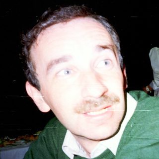 Man with mustache looking off-camera, blurred background.