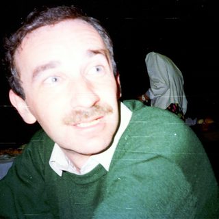 Man with mustache looking off-camera, blurred background.