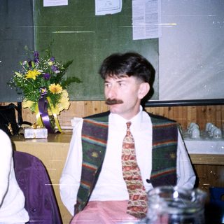 Two people sit with a floral arrangement nearby.