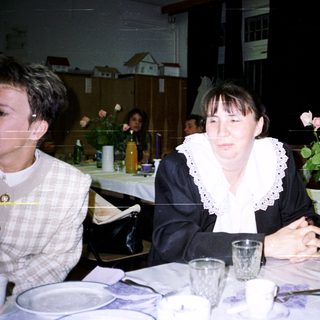 Woman sits at a table with tableware and floral display.