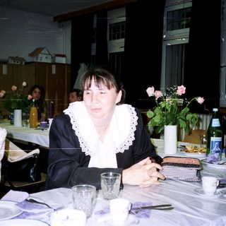 Woman sits at a table with tableware and floral display.