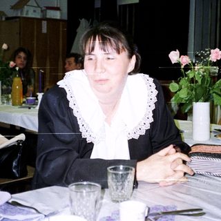Woman sits at a table with tableware and floral display.