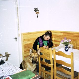 Woman writes at a table with a German Shepherd nearby.