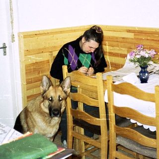 Woman writes at a table with a German Shepherd nearby.