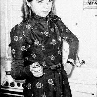 Woman in floral dress stands in a vintage kitchen.