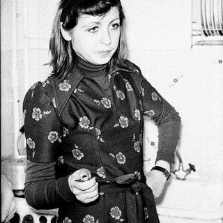 Woman in floral dress stands in a vintage kitchen.