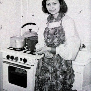 Woman in kitchen, preparing food near a stove.