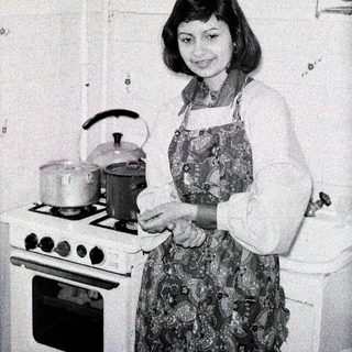 Woman in kitchen, preparing food near a stove.