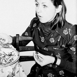 Here's a brief summary of the image: Young woman seated, looking off to the side, holding a small object.