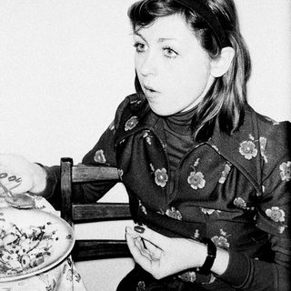 Here's a brief summary of the image: Young woman seated, looking off to the side, holding a small object.