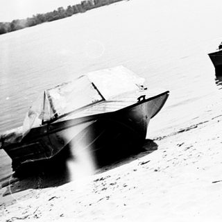 Here's a brief summary of the image: Boats sit on a sandy shore, with a person in one.