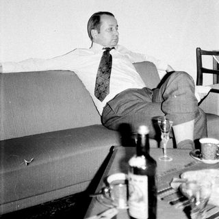 Man relaxes on a couch with drinks and artwork.