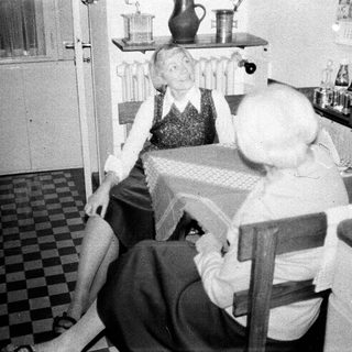 Here's a brief summary of the image: Woman seated in a kitchen, appearing distressed or unwell.