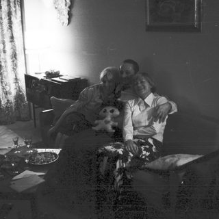 Couple relaxes on couch with child in a dimly lit room.