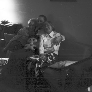Couple relaxes on couch with child in a dimly lit room.