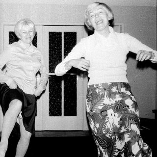 Two women playfully pose near a door in a hallway.