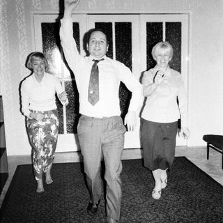 Man raises hand between two women in patterned clothing.