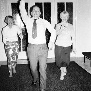 Man raises hand between two women in patterned clothing.