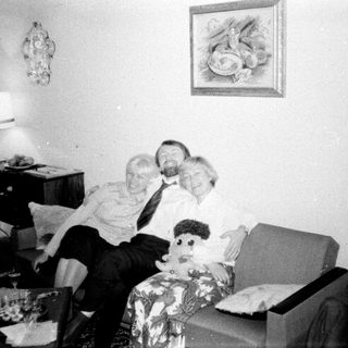 Man, woman, and doll sit on a patterned armchair.