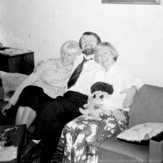 Man, woman, and doll sit on a patterned armchair.