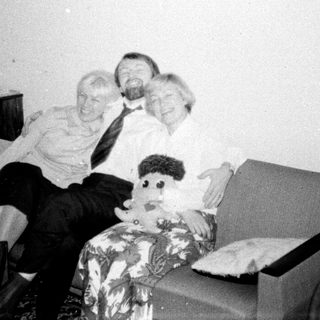 Man, woman, and doll sit on a patterned armchair.