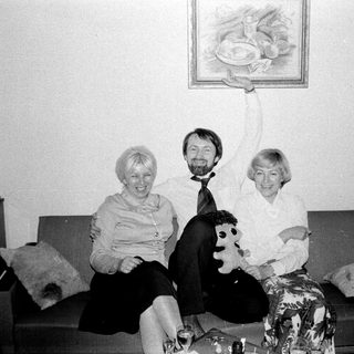 Here's a brief summary of the image: Three people sit on a couch; one holds a painting.