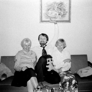 Here's a brief summary of the image: Three people sit on a couch; one holds a painting.