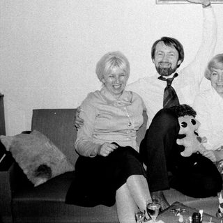 Here's a brief summary of the image: Three people sit on a couch; one holds a painting.