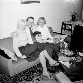 Here's a brief summary of the image: Three people seated on a sofa, in a vintage living room.