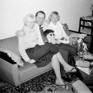 Here's a brief summary of the image: Three people seated on a sofa, in a vintage living room.