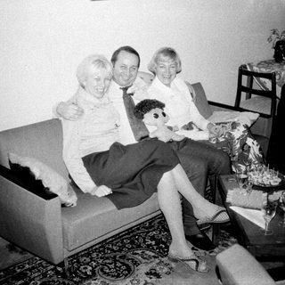 Here's a brief summary of the image: Three people seated on a sofa, in a vintage living room.