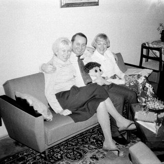 Here's a brief summary of the image: Three people seated on a sofa, in a vintage living room.