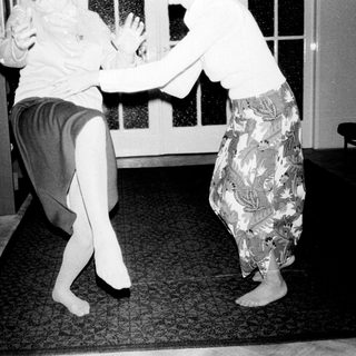 Two women in patterned skirts appear to be dancing.