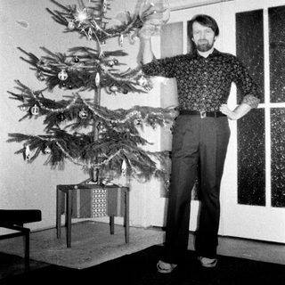 Man stands near a decorated Christmas tree indoors.