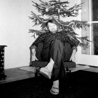 Man sits with head through a small, decorated Christmas tree.