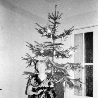Woman sits under a small, decorated Christmas tree.
