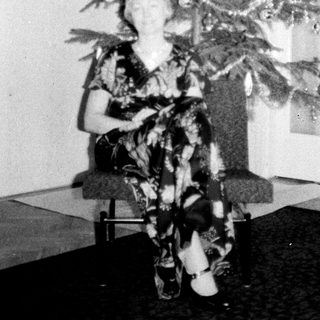 Woman sits under a small, decorated Christmas tree.
