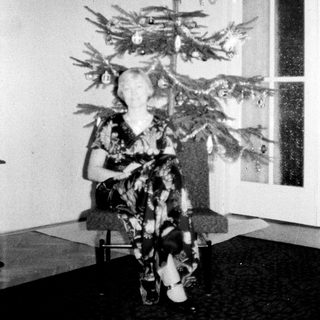 Woman sits under a small, decorated Christmas tree.