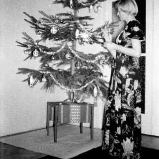 Woman decorating a small Christmas tree indoors.