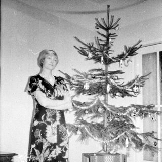 Woman stands near a small, decorated Christmas tree.