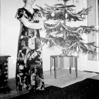 Woman stands near a small, decorated Christmas tree.