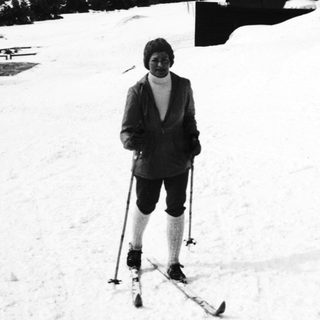 Man on skis stands near a snowy, rustic cabin.