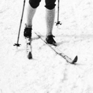 Man on skis stands near a snowy, rustic cabin.